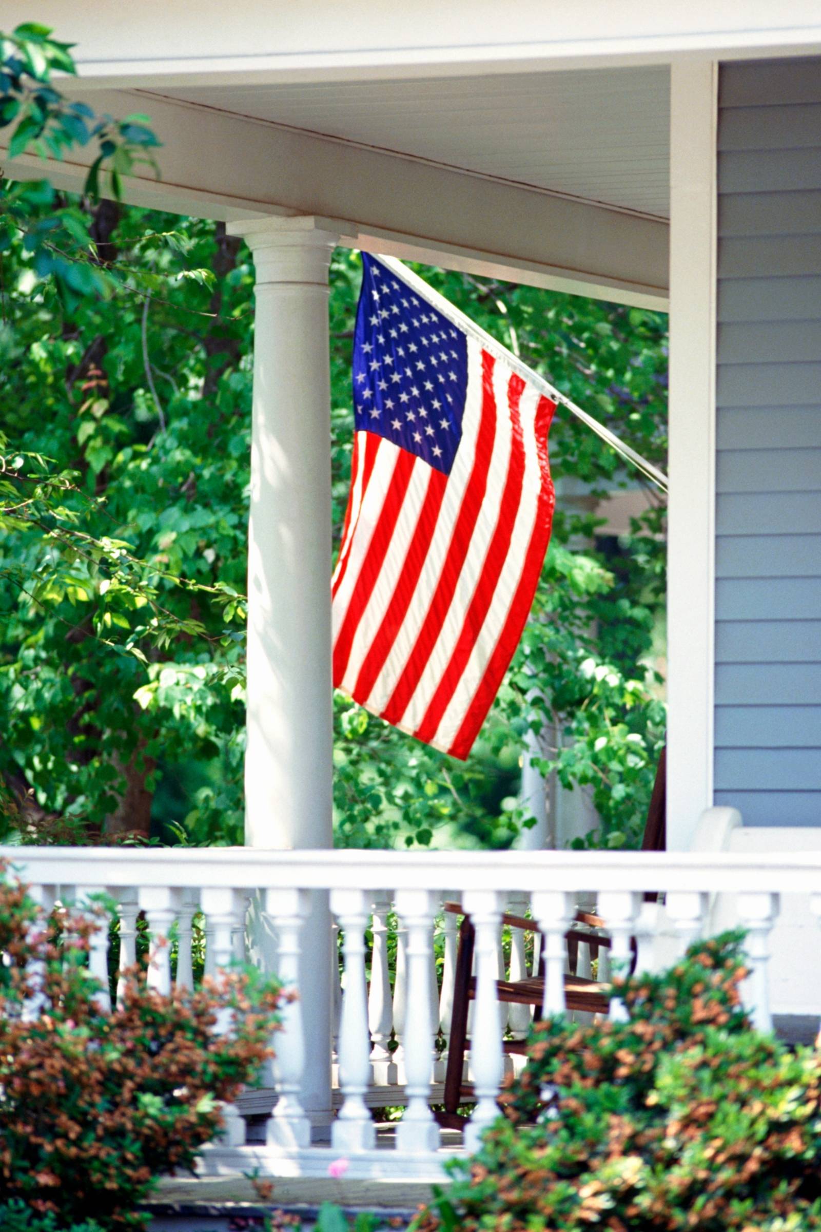 American flag on a residential front porch, framed by greenery