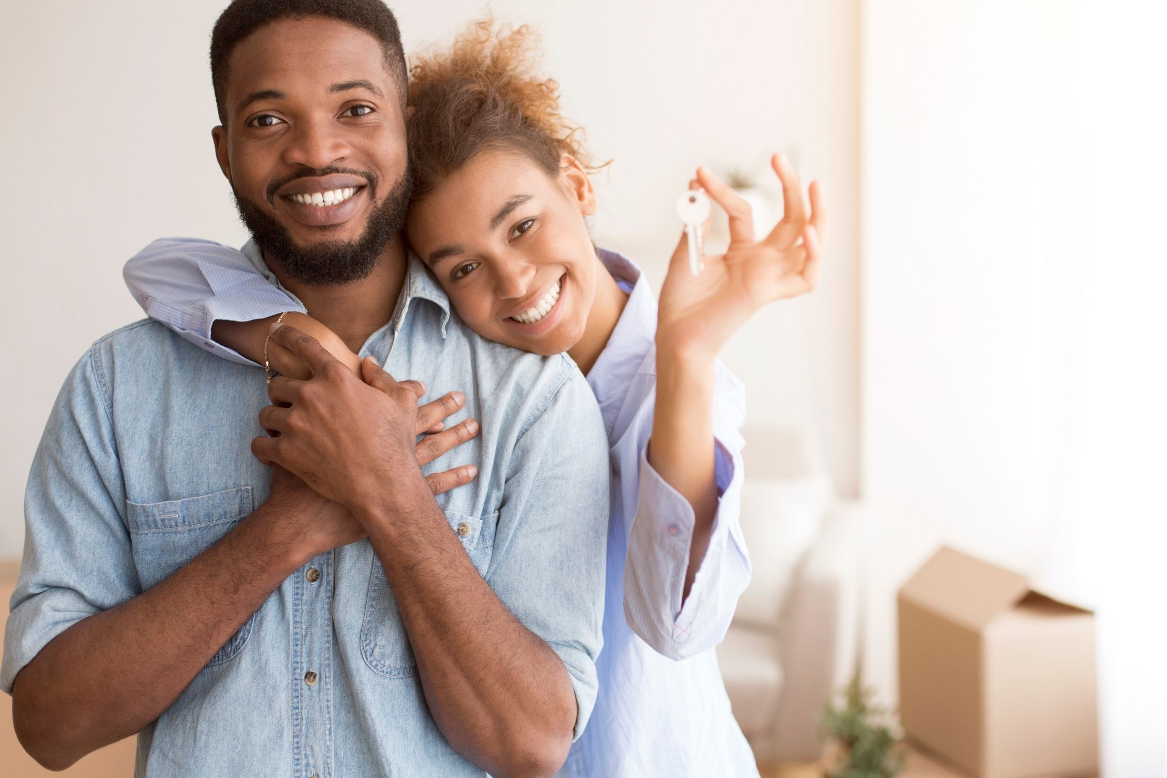 Young couple holding a new house key, surrounded by moving boxes